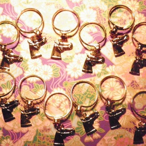 May include: Gold-colored keychains with a horse head pendant. The keychains have a circular ring and a detailed horse head charm. The background is a floral patterned paper in shades of purple, pink, and white.