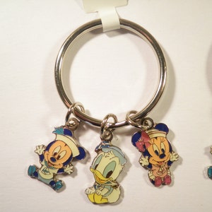 K&ouml;nnte beinhalten: Schl&uuml;sselanh&auml;nger mit Mickey Mouse, Minnie Mouse und Donald Duck in Matrosenoutfits. Die Anh&auml;nger sind farbig emailliert auf silberfarbenem Metall, befestigt an einem gro&szlig;en silbernen Ring. Ein lustiges Sammlerst&uuml;ck.