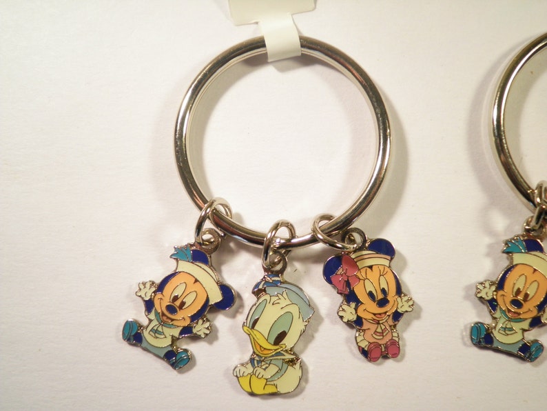 K&ouml;nnte beinhalten: Schl&uuml;sselanh&auml;nger mit Mickey Mouse, Minnie Mouse und Donald Duck in Matrosenoutfits. Die Anh&auml;nger sind farbig emailliert auf silberfarbenem Metall, befestigt an einem gro&szlig;en silbernen Ring. Ein lustiges Sammlerst&uuml;ck.