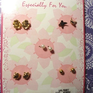 May include: A display card featuring several pairs of earrings. The earrings include gold-toned textured studs, pearl studs, a gold star and a gold butterfly, and small gold ball studs. The card has a floral design and the text "Especially For You".