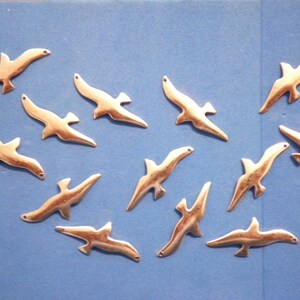 May include: A scattering of small, gold-coloured bird charms, each with a hole for attaching to a project. The charms are arranged on a blue background. Ideal for jewellery making or craft projects.