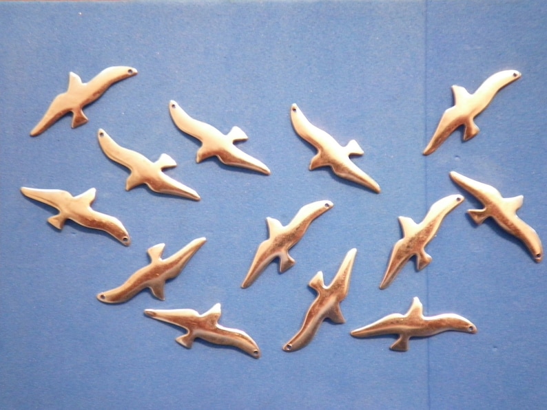 May include: A scattering of small, gold-coloured bird charms, each with a hole for attaching to a project. The charms are arranged on a blue background. Ideal for jewellery making or craft projects.