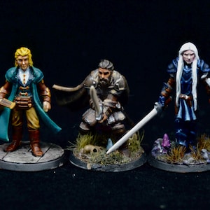 May include: Three hand-painted miniature figurines standing on circular bases. The left figure wears a teal coat and yellow pants. The center figure is a bearded warrior in brown armor holding a sword. The right figure has long white hair and blue armor.