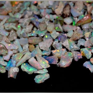 May include: A collection of raw, unpolished opal stones featuring a milky white base with iridescent flashes of green, blue, orange, and red. The small, irregular fragments display a natural, rough texture with varying levels of translucency.