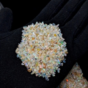 May include: A collection of small, irregular, translucent opal chips featuring a spectrum of iridescent colors including flashes of blue, green, yellow, and orange. The tiny, polished gemstone fragments are clustered together in a dense pile.