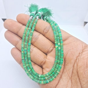 May include: Three strands of small, round, translucent green beads with iridescent flecks. Each strand is finished with a small, matching green thread tassel secured by a silver-toned metal cap at the top of the bead arrangement.