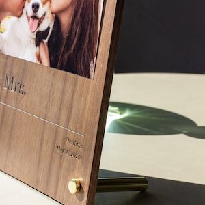 May include: A wooden photo frame with a picture of a couple and their dog. The frame is engraved with "Mrs." and "The Kirins May 16, 2020".
