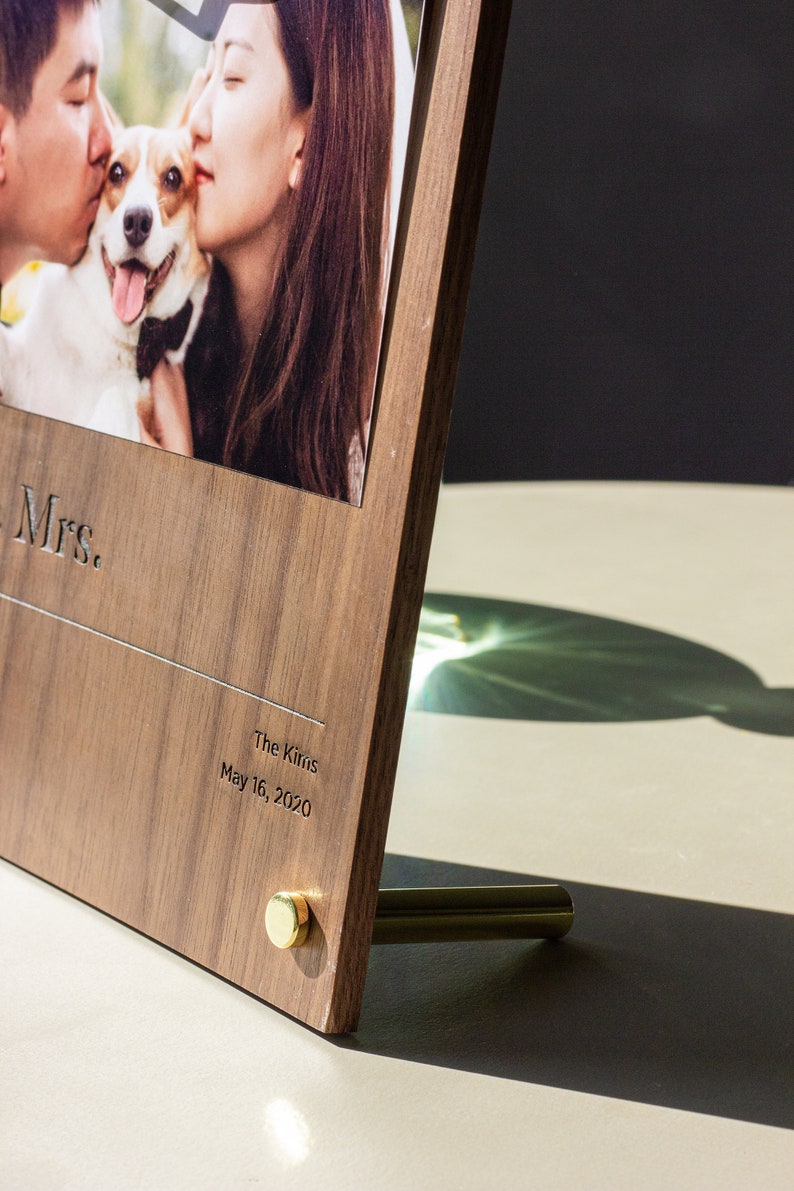 May include: A wooden photo frame with a picture of a couple and their dog. The frame is engraved with "Mrs." and "The Kirins May 16, 2020".