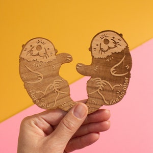 May include: Two wooden otter figurines holding hands, one says "I love you" and the other says "Like no otter".