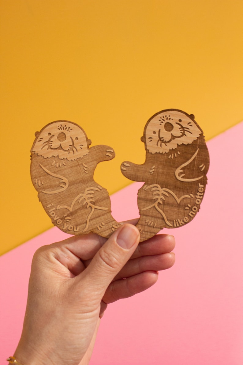May include: Two wooden otter figurines holding hands, one says "I love you" and the other says "Like no otter".