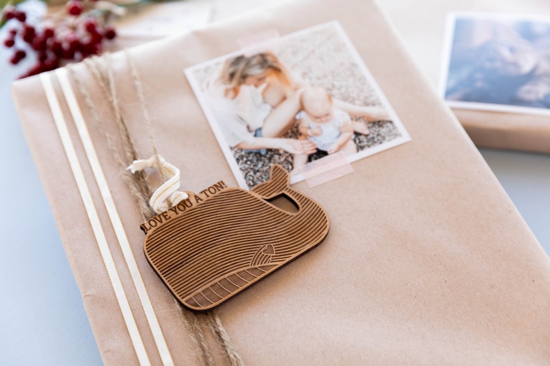 May include: A brown paper gift bag with a wooden whale ornament attached. The ornament has the text "I love you a ton!" engraved on it. The bag is decorated with white twine and a photo of a mother and child.