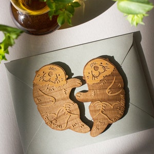 May include: Two wooden otter figurines holding each other, with the text "I love you like no otter" on one and "I love you" on the other.