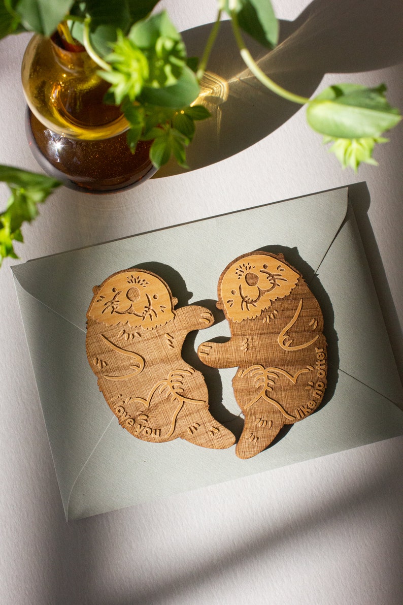 May include: Two wooden otter figurines holding each other, with the text "I love you like no otter" on one and "I love you" on the other.