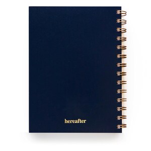 Puede incluir: Un cuaderno azul marino con encuadernaci&oacute;n en espiral de alambre dorado. La palabra "hereafter" est&aacute; impresa en dorado en la esquina inferior derecha de la portada. El cuaderno est&aacute; sobre un fondo blanco.