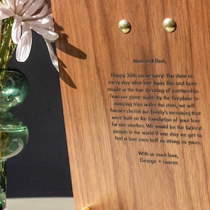 May include: A wooden plaque with an engraved message. The message reads: "Mom and Dad, Happy 30th anniversary! You show us every day what love looks like and have taught us the true meaning of partnership. From our game nights by the fireplace to camping trips under the stars, we will forever cherish our family's memories that were built on the foundation of your love for one another. We would be the luckiest people in the world if one day we get to feel a love even half as strong as yours. With so much love, George + Lauren"