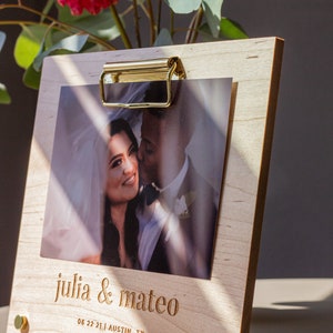 May include: A wooden photo frame with a gold clip, holding a wedding photo of a couple. The frame has the text "julia & mateo" and "06 22 21 | AUSTIN, TX" engraved on it.