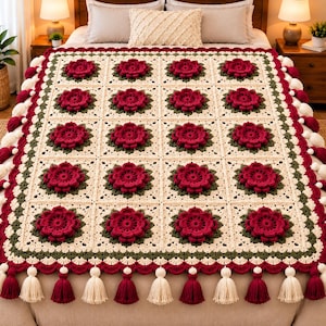 Può includere: Una coperta all'uncinetto color crema con una griglia di motivi quadrati, ognuno centrato con un fiore tridimensionale rosso scuro circondato da foglie verde scuro. I bordi sono rifiniti con un bordo smerlato e nappe alternate.
