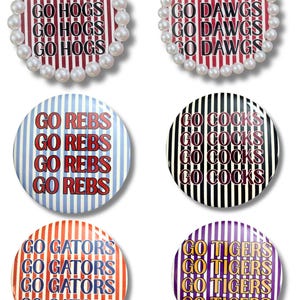 May include: Six circular pin-back buttons featuring vertical striped backgrounds in various colors. Two buttons are bordered with white faux pearls. The text reads GO HOGS, GO DAWGS, GO REBS, GO COCKS, GO GATORS, and GO TIGERS in repeating lines.