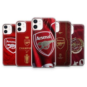May include: Five clear smartphone cases featuring various Arsenal Football Club designs. The cases display the Arsenal crest, the text "Arsenal", "CHAMPION 2025-2026", a trophy icon, a crown, and the Champions League logo in red, white, and gold color schemes.