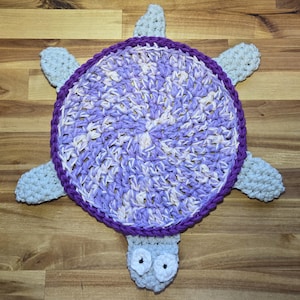 Peut inclure: Un tapis en crochet en forme de tortue avec une carapace circulaire en fil panaché violet clair et blanc, bordée d'une bordure violet foncé. La tête et les quatre nageoires sont en fil gris clair, avec deux petits yeux circulaires noirs.