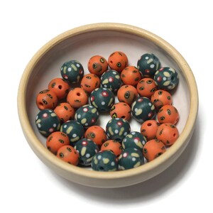 May include: A bowl filled with orange and green patterned beads. The beads are made of clay and have a speckled finish.