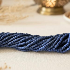 Op de afbeelding: Een lange streng van kleine, matte, donkerblauwe schijfvormige kralen gerangschikt in een horizontale lijn. De kralen hebben een uniforme, ronde vorm met een plat profiel en een consistente diepblauwe kleur over de gehele lengte van de streng.