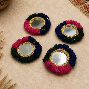 Puede incluir: Cuatro parches circulares bordados con espejos redondos centrales enmarcados por hilo metálico dorado. Cada parche está bordeado por segmentos de hilo grueso cosidos a mano en bloques alternos de verde oscuro, azul marino y rosa magenta vibrante.