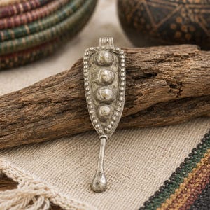 May include: A silver-toned metal pendant featuring a triangular shape with a beaded border and four raised circular elements arranged vertically. The piece includes a narrow, elongated stem extending from the bottom, ending in a small teardrop shape.