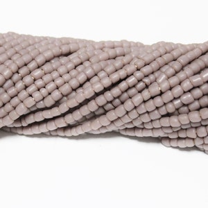 May include: A strand of light grey seed beads. The beads are small and uniform in size and shape.