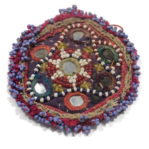 Op de afbeelding: Een ronde, kleurrijke, geborduurde patch met een centraal ontwerp van spiegels en kralen. De patch is omgeven door een franje van blauwe en rode kralen.