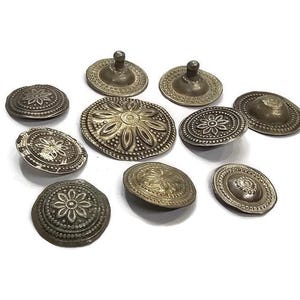 May include: Nine silver-toned metal buttons with intricate floral designs. The buttons are round and have a raised center with a floral pattern.