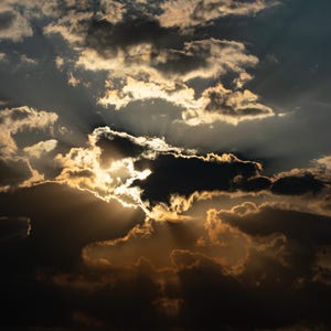 May include: A dramatic sky filled with dark, heavy clouds contrasted by bright golden sunlight breaking through the gaps. The sun rays create a distinct crepuscular effect, illuminating the edges of the clouds with a warm, glowing light.