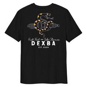 May include: A black t-shirt featuring a white and orange graphic of a snake coiled around a spark plug. Below the graphic, the text reads: Ride Fast and Take Chances, DEXBA, and EST. 2024. The design is centred on the back of the shirt.