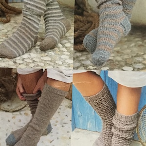 Könnte beinhalten: Vier Paar gestrickte Socken in verschiedenen Stilen und Farben. Ein Paar hat horizontale Streifen, ein anderes ein gesprenkeltes Muster, und zwei sind einfarbig. Die Socken sind in Grau-, Braun- und Blautönen gehalten und zeigen verschiedene Texturen und Designs.