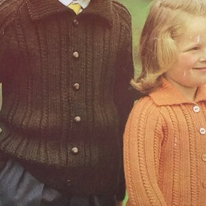 May include: Two children wearing knitted cardigans. The boy is wearing a dark brown cardigan with buttons and the girl is wearing a light orange cardigan with buttons.