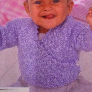 May include: A baby wearing a purple knitted wrap cardigan with a tie closure.