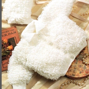 Könnte beinhalten: Weißer gestrickter Baby-Cardigan und passende Mütze mit einer strukturierten, flauschigen Optik. Der Cardigan hat einen Knopfverschluss und die Mütze einen umgeschlagenen Rand.