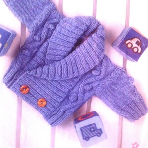 May include: A light purple knitted baby cardigan with a shawl collar and two buttons. The cardigan has a cable knit pattern and is made with soft yarn.