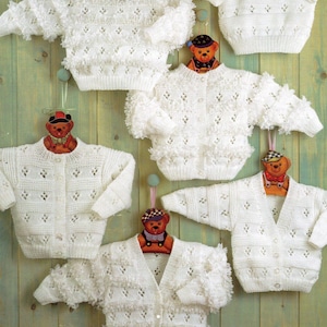 May include: Five white crocheted baby sweaters with a lacy pattern. The sweaters are hanging on wooden hangers with teddy bear decorations.