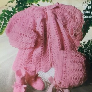 Op de afbeelding: Een roze gehaakte baby-outfit met bijpassende muts en slofjes. De outfit heeft een kantpatroon en is gemaakt van 3-draads garen.