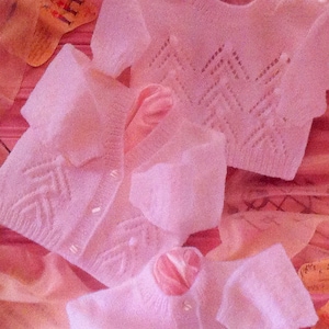 Op de afbeelding: Drie roze gebreide babytruien met een chevron-patroon. De truien zijn gemaakt van zacht, delicaat garen en hebben een klassiek, tijdloos ontwerp.