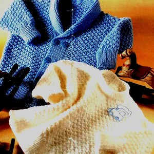 Könnte beinhalten: Zwei gestrickte Babysweater, einer blau und einer weiß. Der blaue Pullover hat einen Schalkragen und ist mit einem strukturierten Stich gearbeitet. Der weiße Pullover hat eine Auto-Applikation auf der Vorderseite.