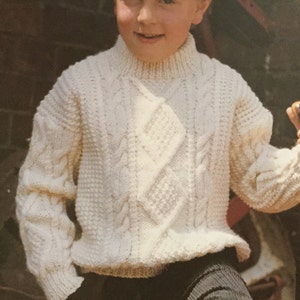 May include: A white knitted sweater with a cable knit pattern. The sweater has a high neck and long sleeves.