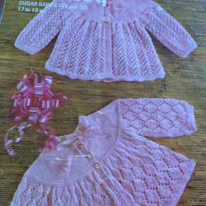 May include: Two pink knitted baby sweaters with a lacy pattern. The sweaters have button closures and are made with a delicate yarn.