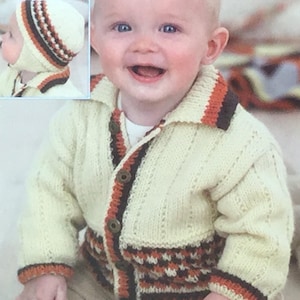 May include: A cream colored knitted cardigan with brown, orange, and white trim. The cardigan has a button closure and a collar. The cardigan is being worn by a baby.