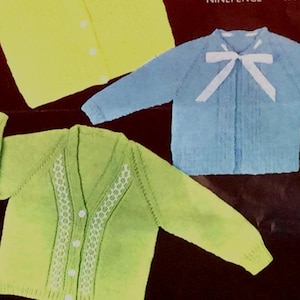 May include: Three knitted cardigans for babies. One is yellow, one is light blue with a white bow, and one is green with white trim.