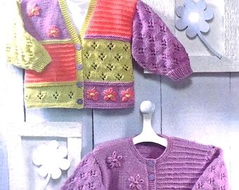 May include: Two knitted baby cardigans with button fastenings. The top cardigan is multicoloured with a green, orange and purple colour scheme. The bottom cardigan is a solid purple colour. Both cardigans have flower embellishments.