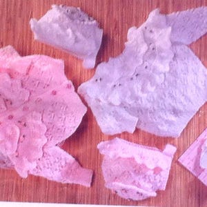 May include: Four crocheted baby sweaters in pink and white. Two of the sweaters are pink with a floral design and two are white with a ruffled design.
