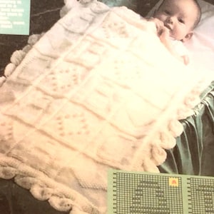 Puede incluir: Una manta de bebé de ganchillo blanco con un borde festoneado. La manta está colocada en una cuna con un bebé acostado encima.