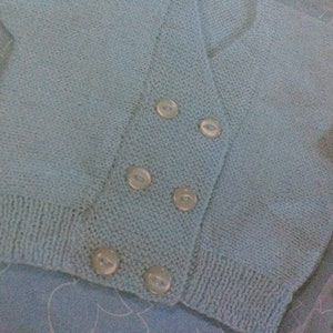 May include: A light blue knitted cardigan with a double breasted closure and five white buttons.
